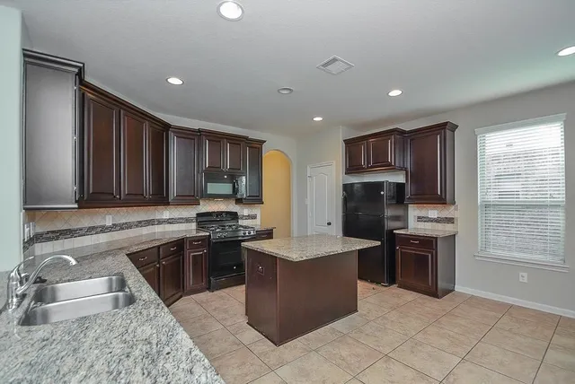 a kitchen with stainless steel appliances granite countertop a stove top oven a sink dishwasher a refrigerator and a oven with wooden cabinets