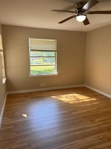 a view of an empty room with wooden floor and a ceiling fan