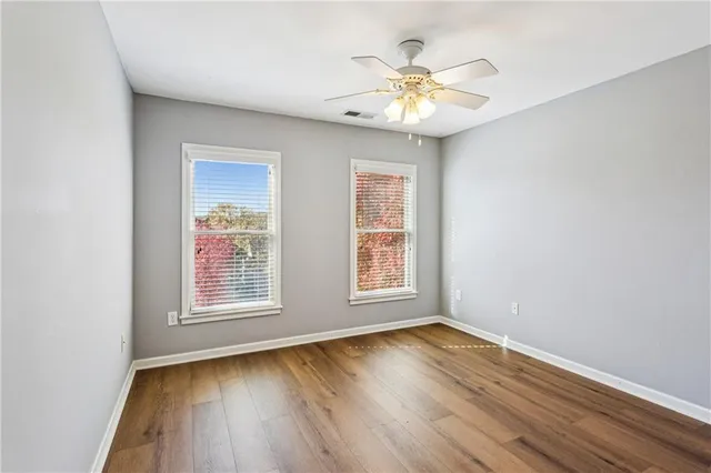 an empty room with wooden floor chandelier fan and windows