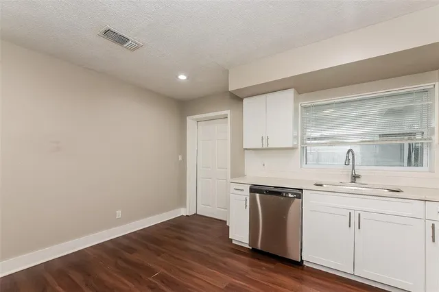 a kitchen with a sink stainless steel appliances white cabinets and wooden floor
