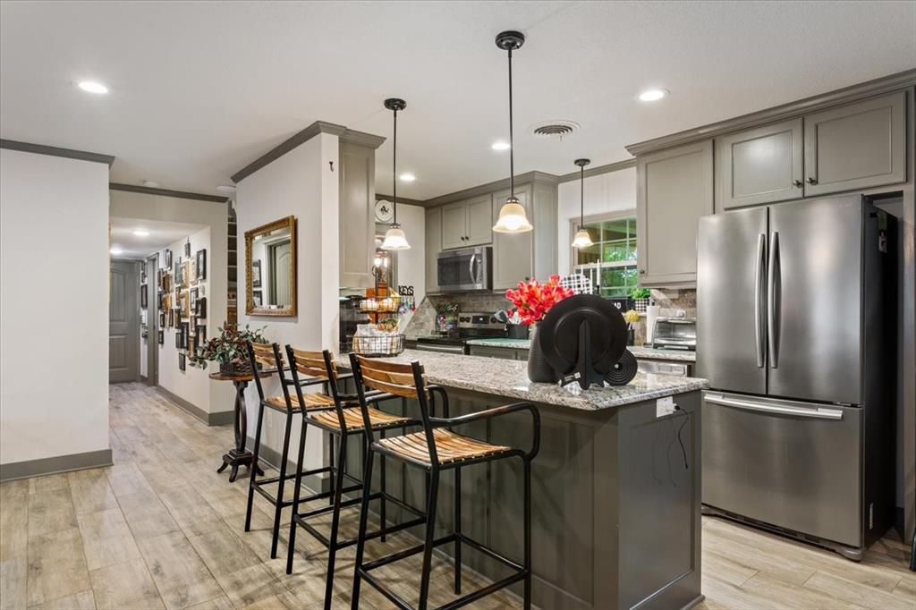 649 Wedgewood Drive China Spring, TX 76633 - Photo 7 of 39 Kitchen featuring gray cabinetry, appliances with stainless steel finishes, light stone counters, a kitchen breakfast bar, and decorative light fixtures