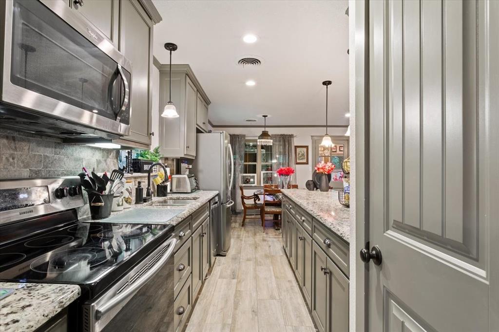 649 Wedgewood Drive China Spring, TX 76633 - Photo 9 of 39 Kitchen featuring appliances with stainless steel finishes, pendant lighting, light stone counters, light wood-style floors, and backsplash