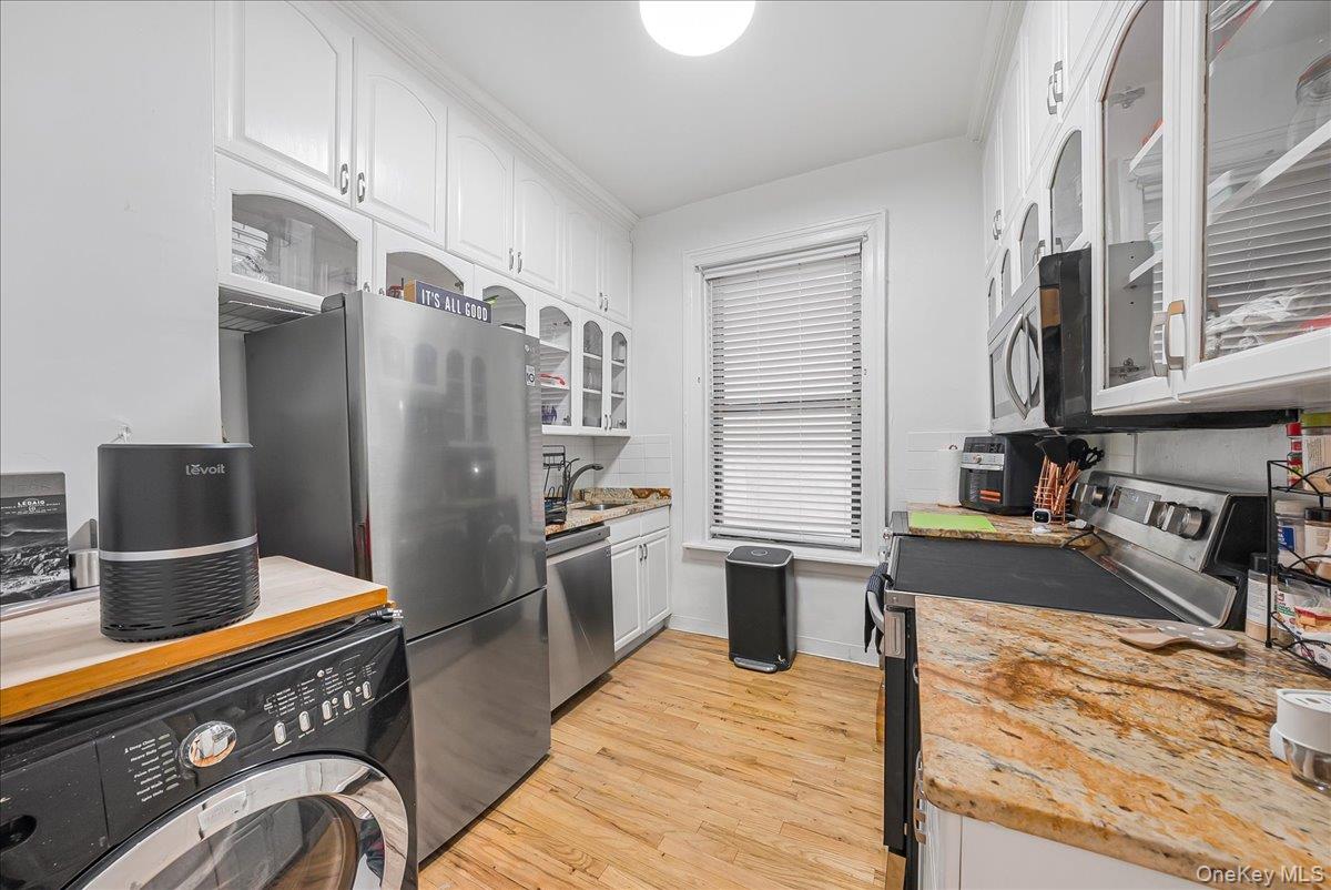 137 West 142nd Street, Unit 4A Manhattan, NY 10030 - Photo 15 of 24 Kitchen with glass insert cabinets, washer / dryer, white cabinets, appliances with stainless steel finishes, and light wood-style flooring