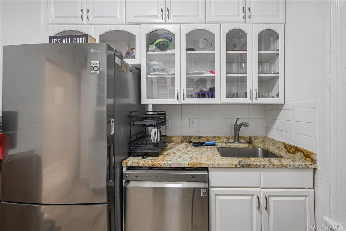 137 West 142nd Street, Unit 4A Manhattan, NY 10030 - Photo 16 of 24 Kitchen with white cabinetry, decorative backsplash, stainless steel appliances, glass insert cabinets, and light stone counters