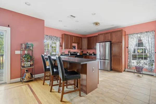 a kitchen with stainless steel appliances kitchen island granite countertop a refrigerator a stove a dining table and chairs with wooden floor