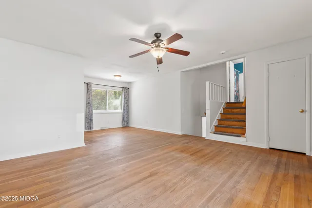 a view of an empty room with wooden floor and a ceiling fan