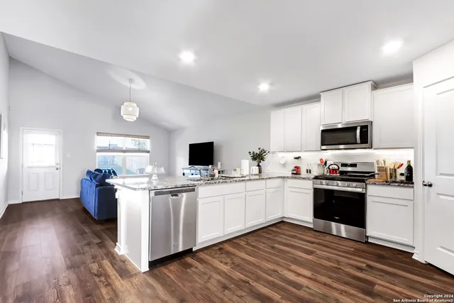 a kitchen with stainless steel appliances kitchen island granite countertop a refrigerator a stove a sink a dining table and chairs with wooden floor