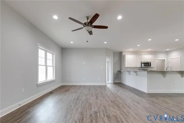 a view of an empty room and kitchen with wooden floor and a window