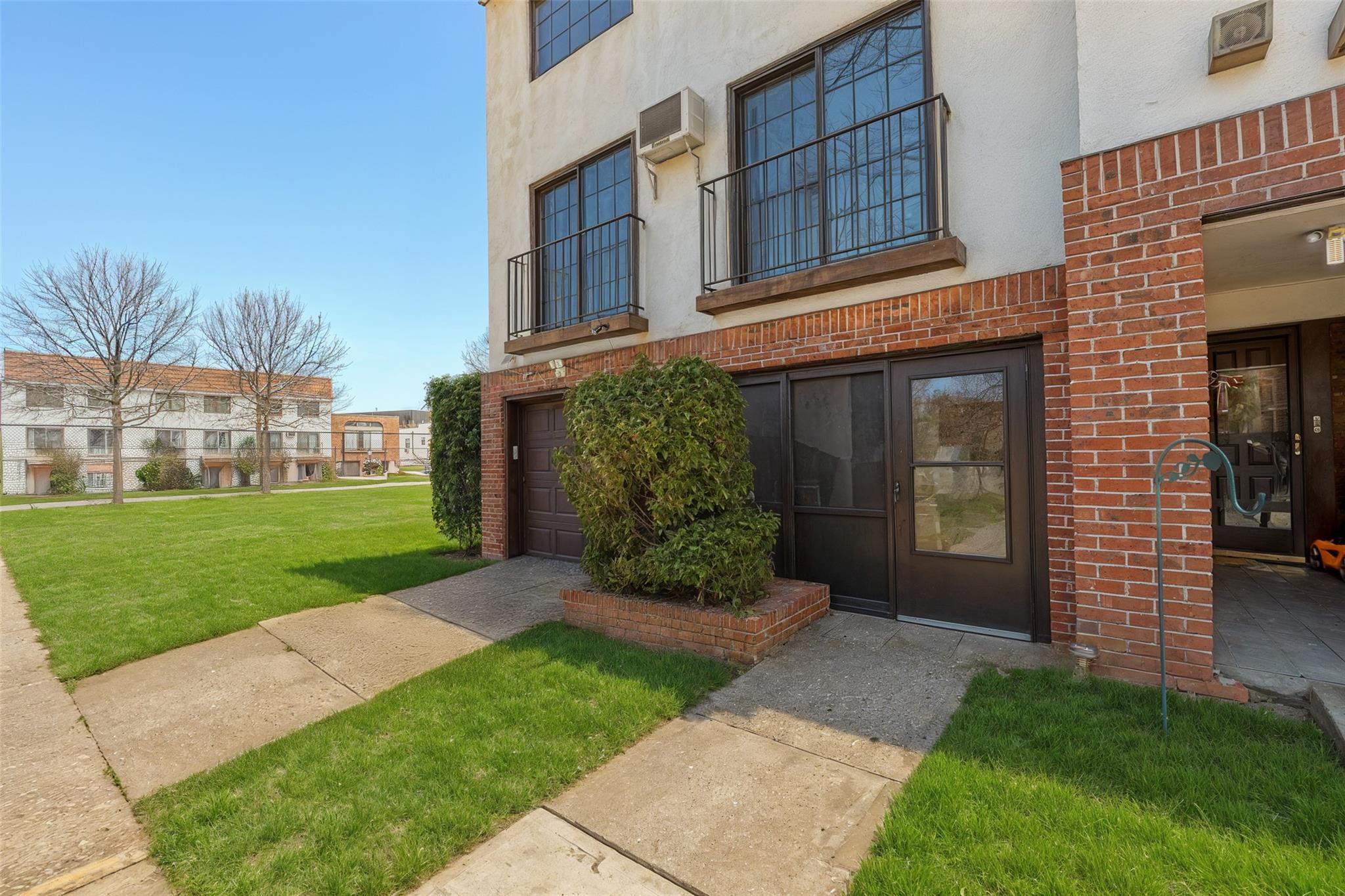 509 Julius Road Queens, NY 11356 - Photo 2 of 26 Property entrance with stucco siding, brick siding, a lawn, and a wall unit AC