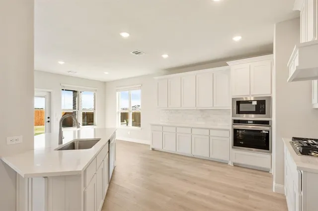 a kitchen with granite countertop a refrigerator oven a sink dishwasher and white cabinets with wooden floor