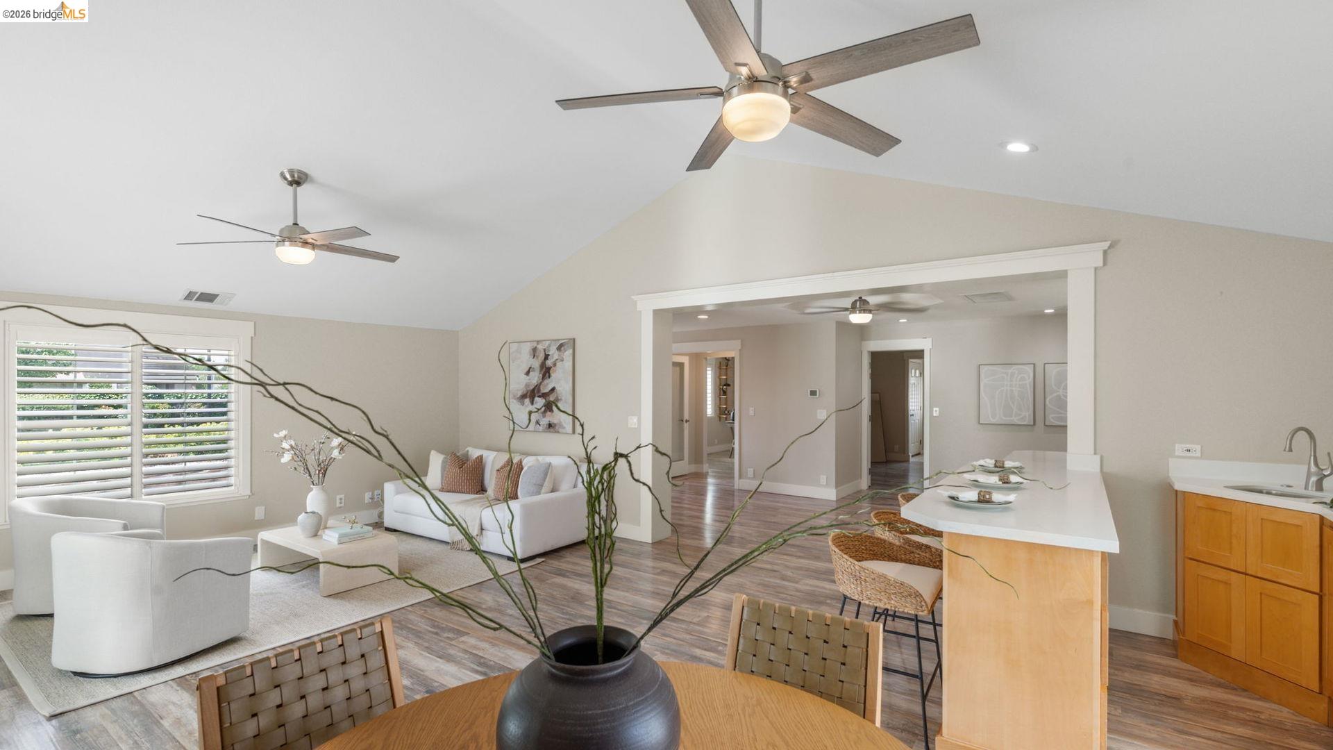 700 Brownstone Road Oakley, CA 94561 - Photo 20 of 58 Open-concept living space featuring wood-finish flooring, vaulted ceilings, plantation shutters, a kitchen island with a white countertop, and light wood cabinetry