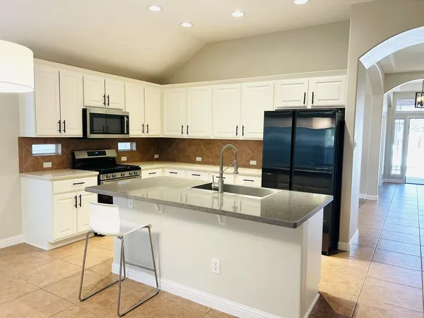 a kitchen with stainless steel appliances kitchen island granite countertop a refrigerator a stove a sink and white cabinets with wooden floor