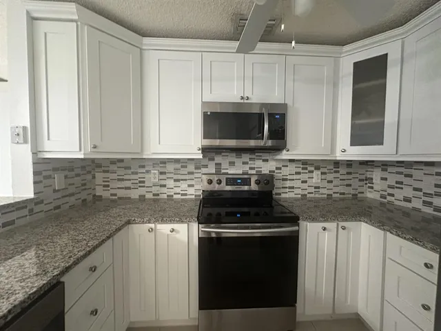 a kitchen with granite countertop white cabinets and stainless steel appliances