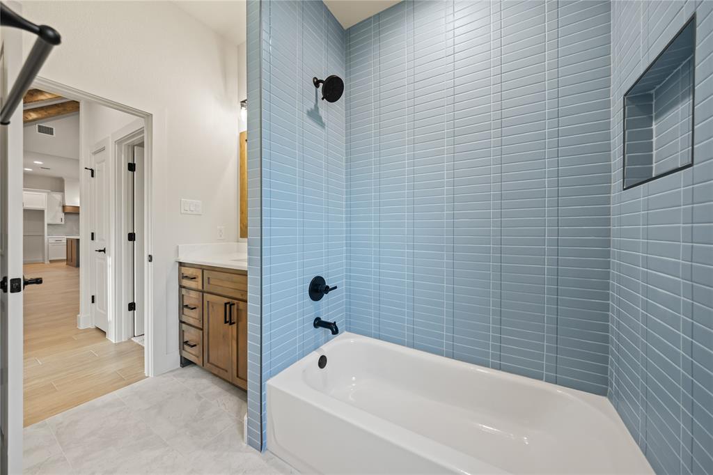 7004 Rnch Vw Place Springtown, TX 76082 - Photo 21 of 25 Bathroom featuring a built-in bathtub, light blue subway tile surround, recessed shower niche, wood-finish vanity with countertop, and black fixtures