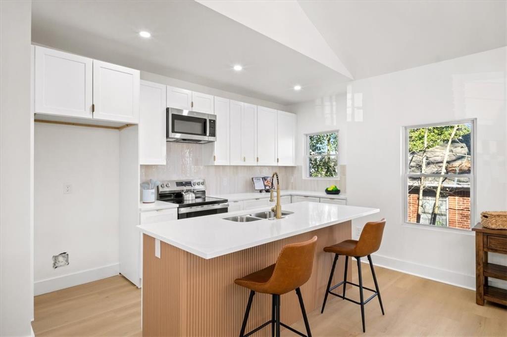 1523 Melrose Drive Southwest Atlanta, GA 30310 - Photo 8 of 33 a kitchen with stainless steel appliances a sink a stove a refrigerator white cabinets and a dining table with wooden floor