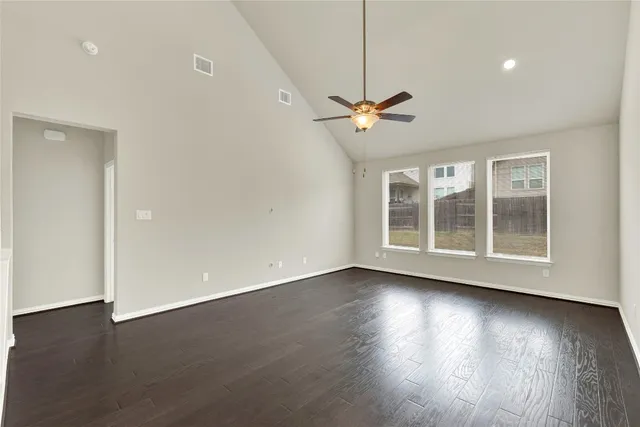 a view of an empty room with wooden floor ceiling fan and a window