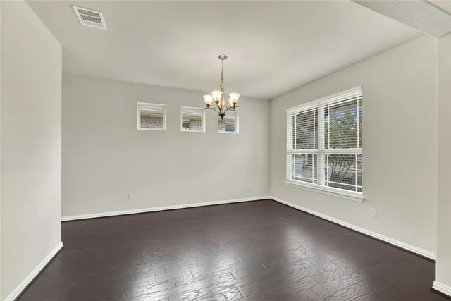 an empty room with wooden floor chandelier and windows