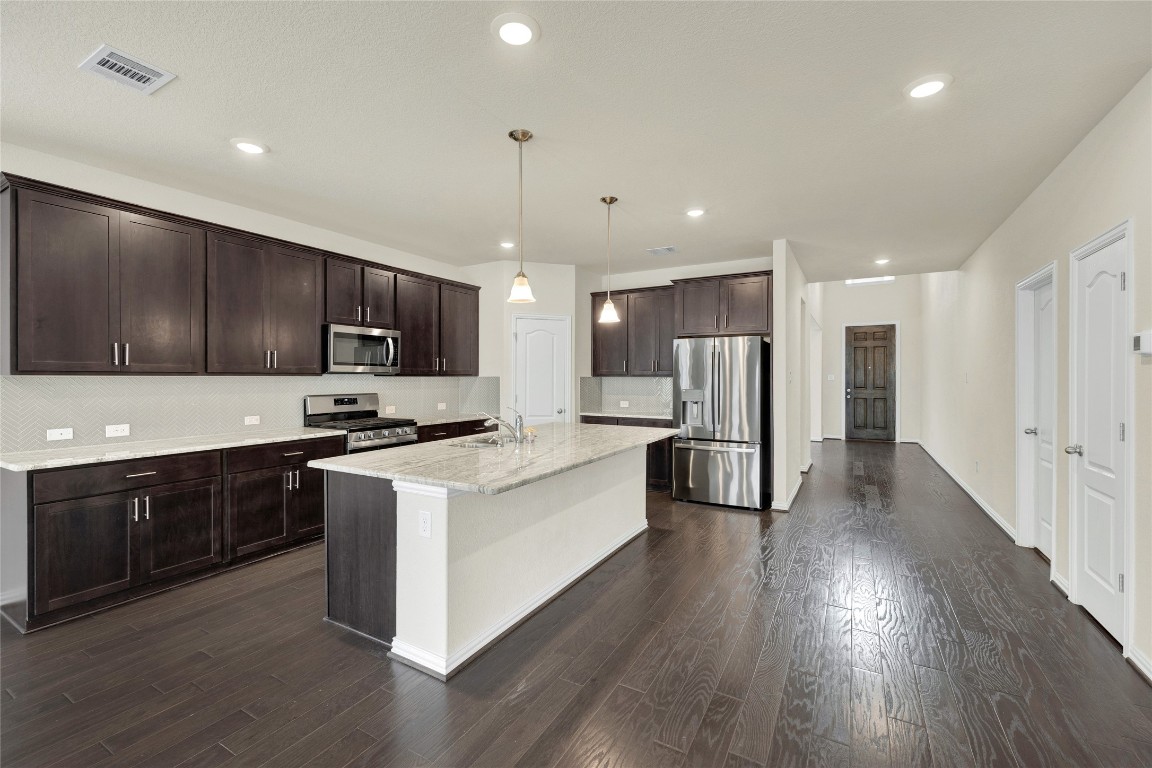 908 Leadtree Loop Buda, TX 78610 - Photo 8 of 38 a large kitchen with stainless steel appliances granite countertop a large center island a stove a refrigerator white cabinets and wooden floor