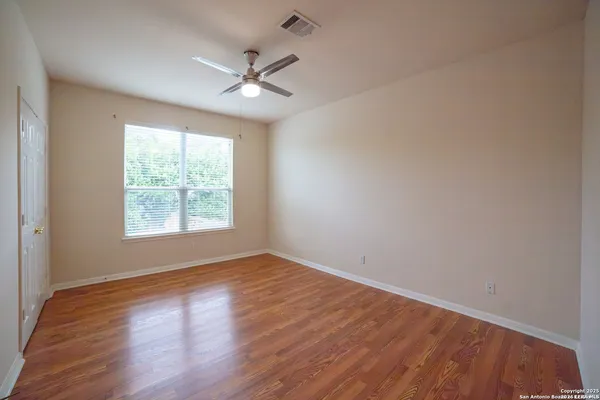 an empty room with wooden floor chandelier fan and windows