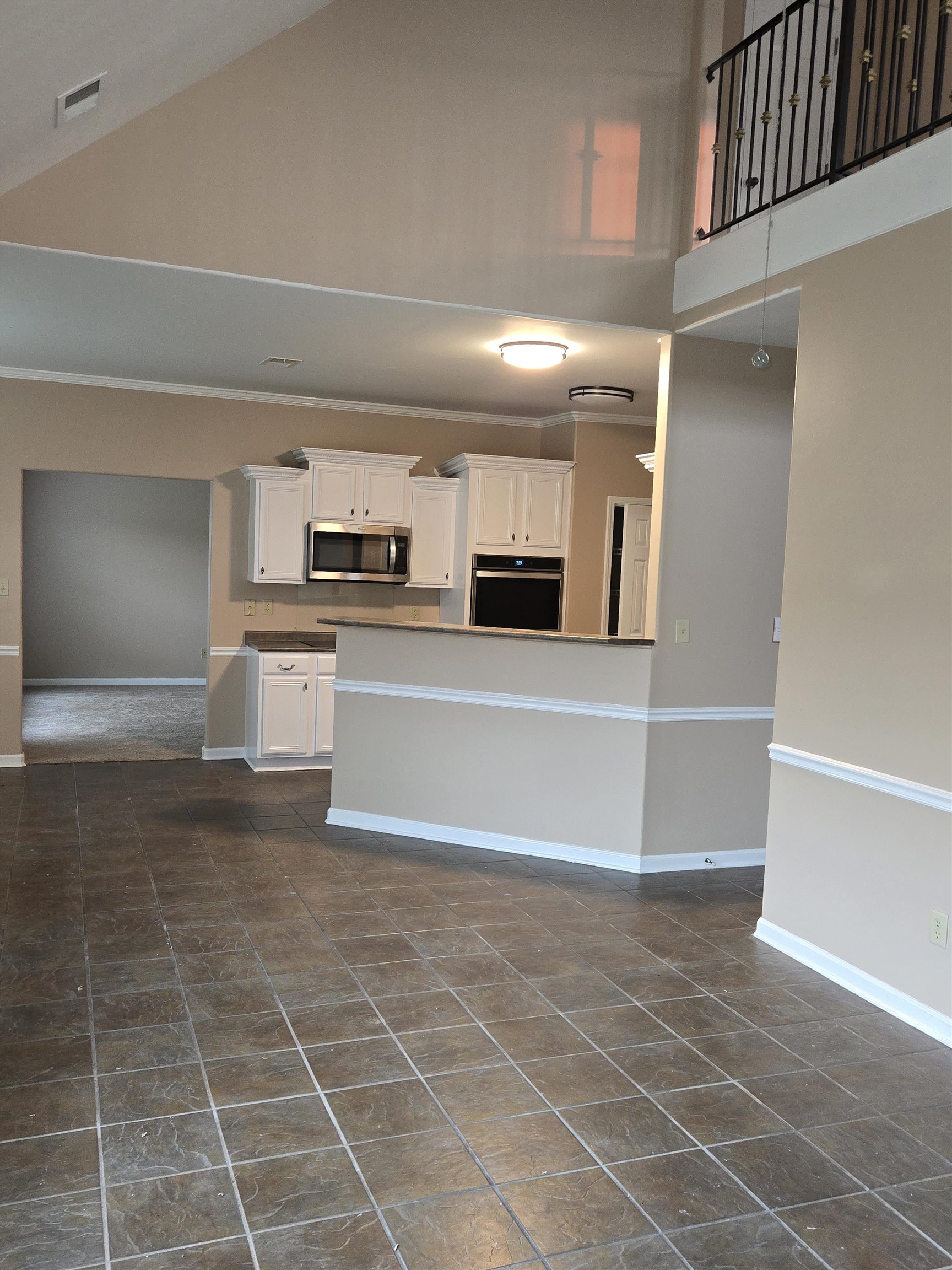 Kitchen with high vaulted ceiling, white cabinetry, black oven, stainless steel microwave, and dark tile patterned flooring
