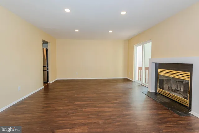 a view of an empty room with wooden floor fireplace and a window