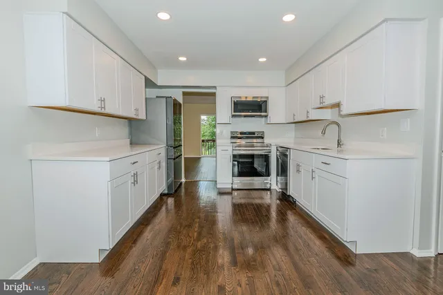 a kitchen with stainless steel appliances a stove top oven a sink a refrigerator white cabinets and wooden floor