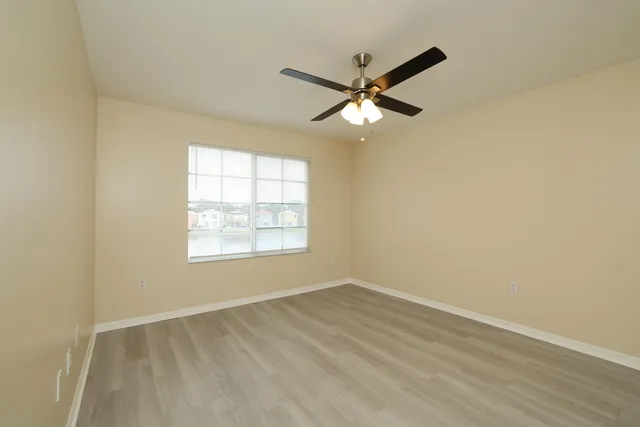 an empty room with wooden floor fan and windows