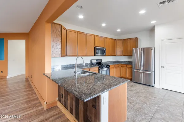 a kitchen with stainless steel appliances granite countertop a stove top oven a sink dishwasher and a refrigerator with wooden cabinets