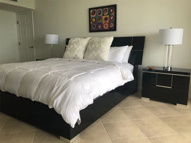 a bedroom with a large bed and a flat tv screen on dresser next to a window