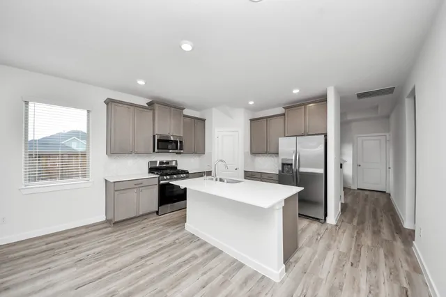 a kitchen with stainless steel appliances kitchen island granite countertop a stove a sink a refrigerator white cabinets and wooden floor