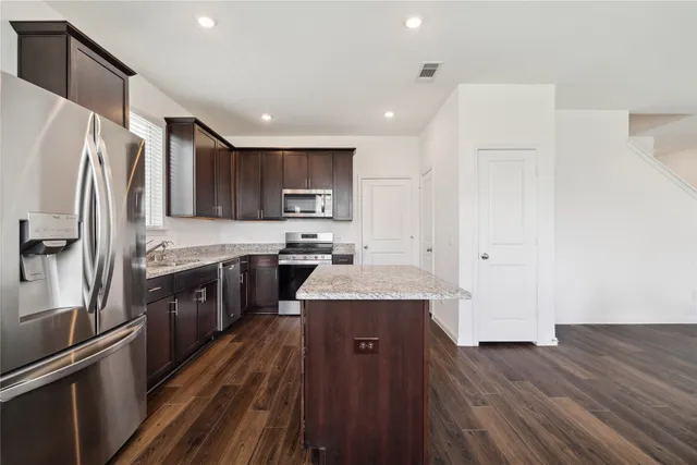 a kitchen with kitchen island granite countertop wooden floors appliances and cabinets