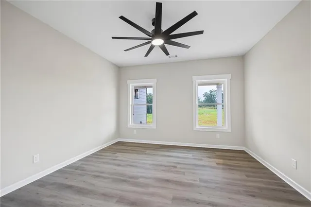 an empty room with wooden floor fan and windows