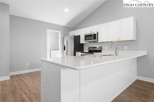 a kitchen with stainless steel appliances a sink a stove a microwave a sink and white cabinets