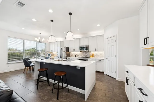 a kitchen with stainless steel appliances kitchen island a table chairs sink and cabinets