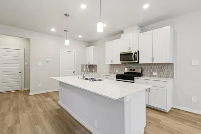 a kitchen with a sink a microwave a stove and white cabinets with wooden floor
