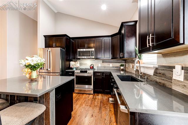 711 Pine Ridge Street Elizabeth, CO 80107 - Photo 18 of 39 Kitchen featuring appliances with stainless steel finishes, vaulted ceiling, light hardwood / wood-style floors, tasteful backsplash, and sink