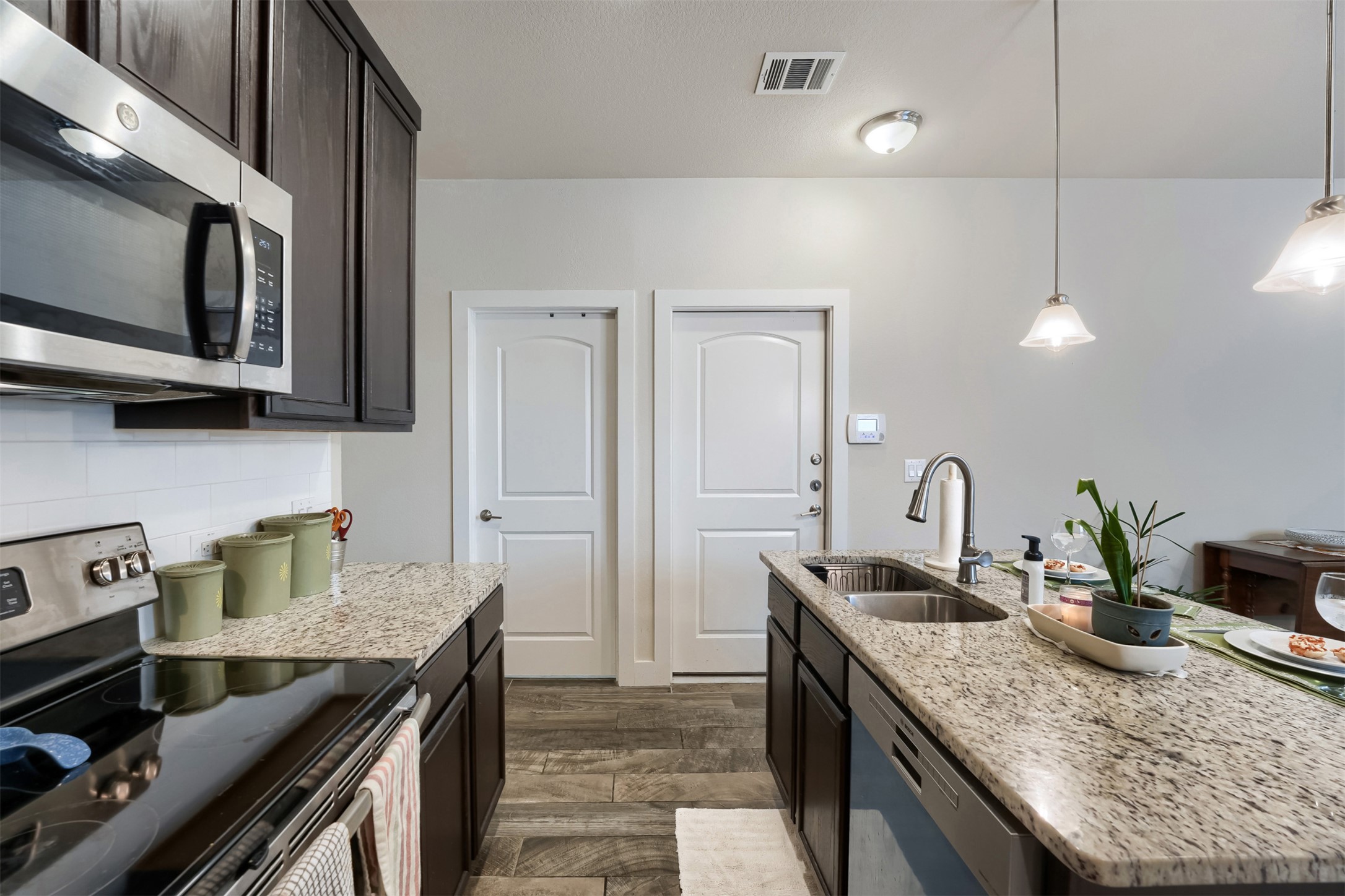 418 High Tech Drive Georgetown, TX 78626 - Photo 12 of 34 Kitchen featuring granite countertops, dark wood cabinetry, a stainless steel over-the-range microwave, and a subway tile backsplash