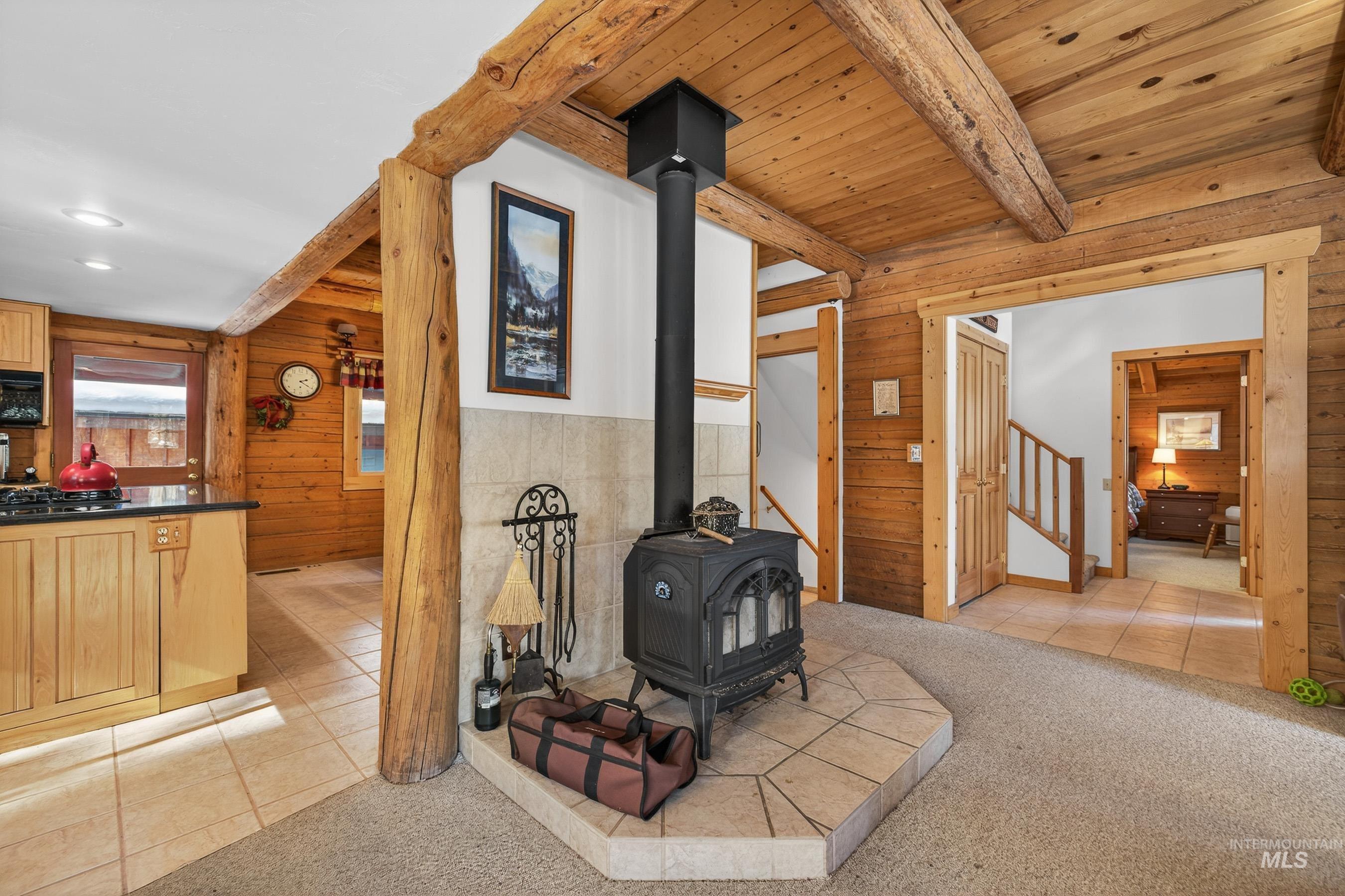 441 Allen Avenue McCall, ID 83638 - Photo 16 of 46 Living room with wooden walls, a wood stove, light colored carpet, light tile patterned floors, and a wood ceiling with exposed beams