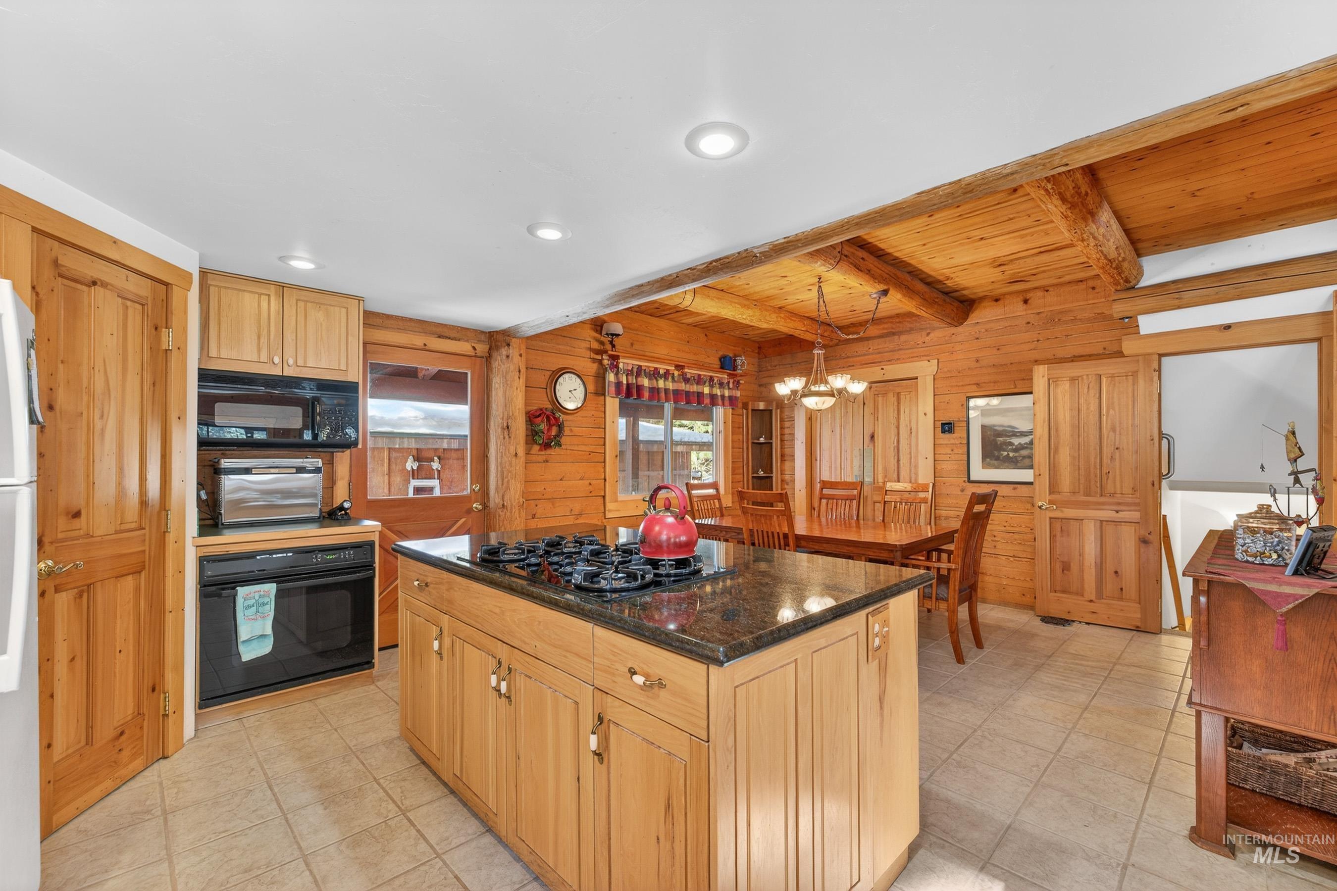 441 Allen Avenue McCall, ID 83638 - Photo 26 of 46 Kitchen featuring wood walls, black appliances, a kitchen island, dark stone countertops, and a chandelier
