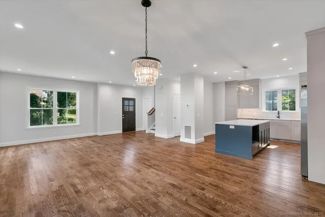 a view of an empty room and kitchen with wooden floor