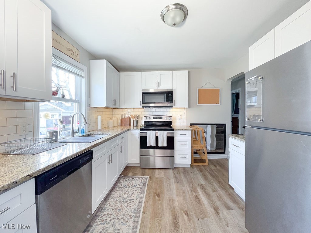 2707 Hearthstone Road Cleveland, OH 44134 - Photo 15 of 49 Kitchen with a sink, light stone countertops, appliances with stainless steel finishes, light wood-style flooring, and decorative backsplash