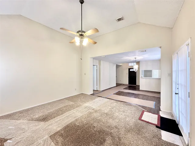 a view of an empty room with chandelier fan and kitchen view