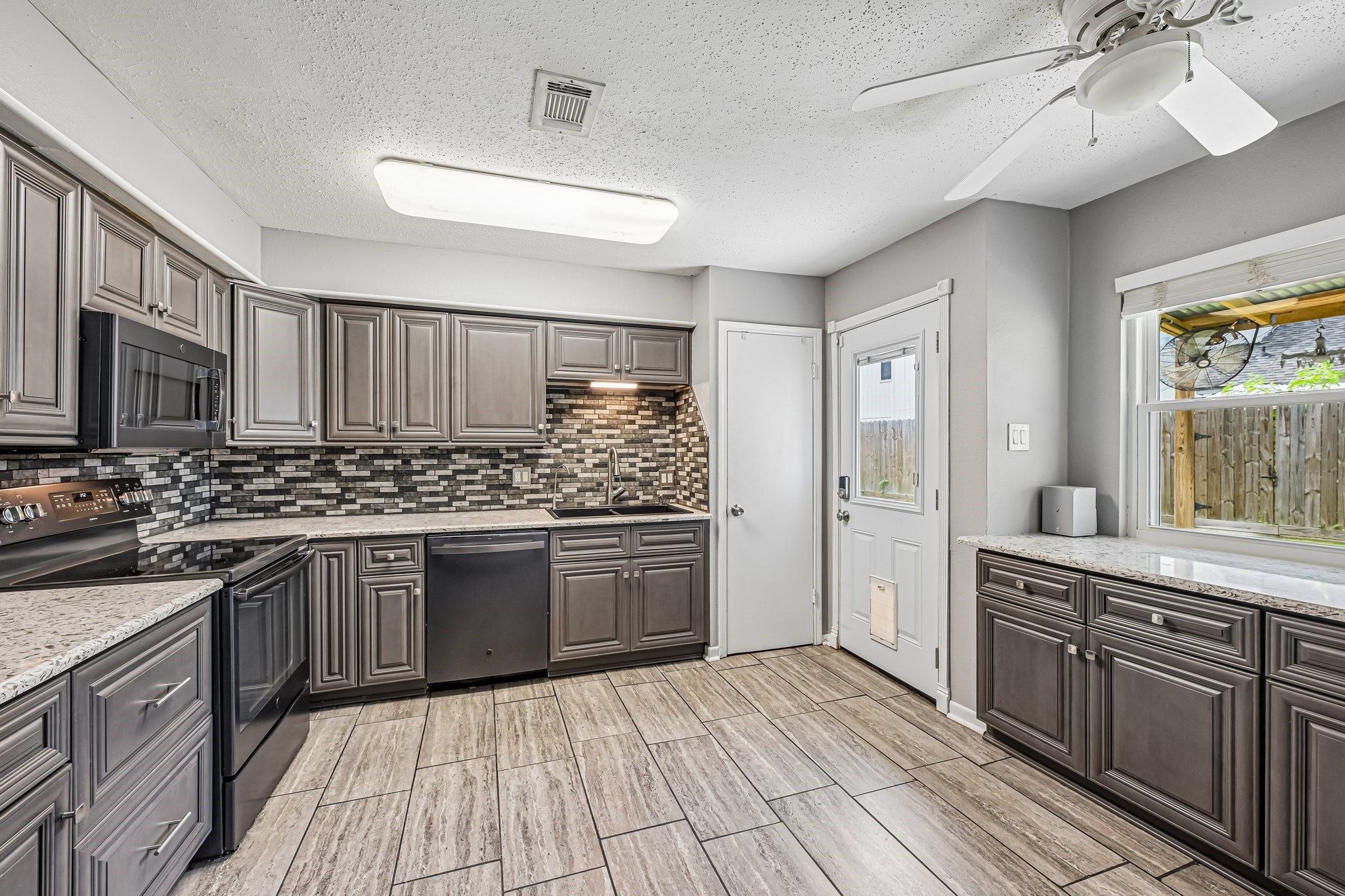 8 Arlington Street Conroe, TX 77301 - Photo 20 of 37 This modern kitchen features sleek gray cabinetry, a stylish tile backsplash, and stainless steel appliances. Ample counter space and a large window provide a bright, open feel, while the door gives easy access to the backyard.
