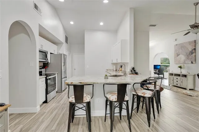 a kitchen with stainless steel appliances kitchen island granite countertop a dining table chairs and a refrigerator