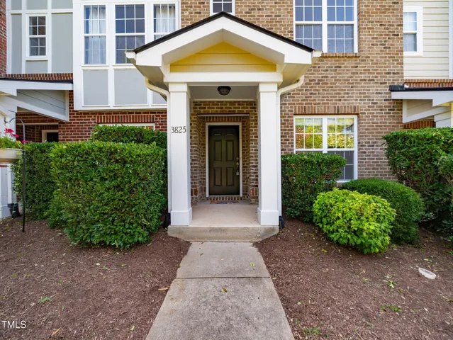 a view of a brick house with potted plants and a yard