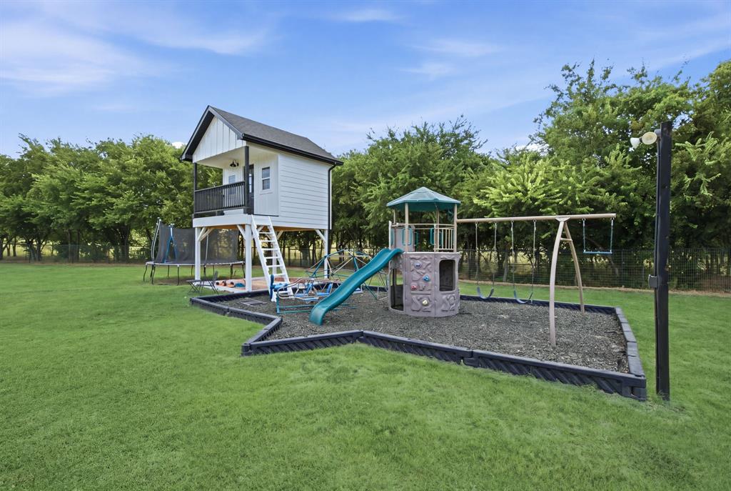 10216 Finch Road Sanger, TX 76266 - Photo 32 of 40 Expansive grass lawn featuring a play structure with a slide and swings, and a raised playhouse with an exterior staircase and porch - Virtual Grass