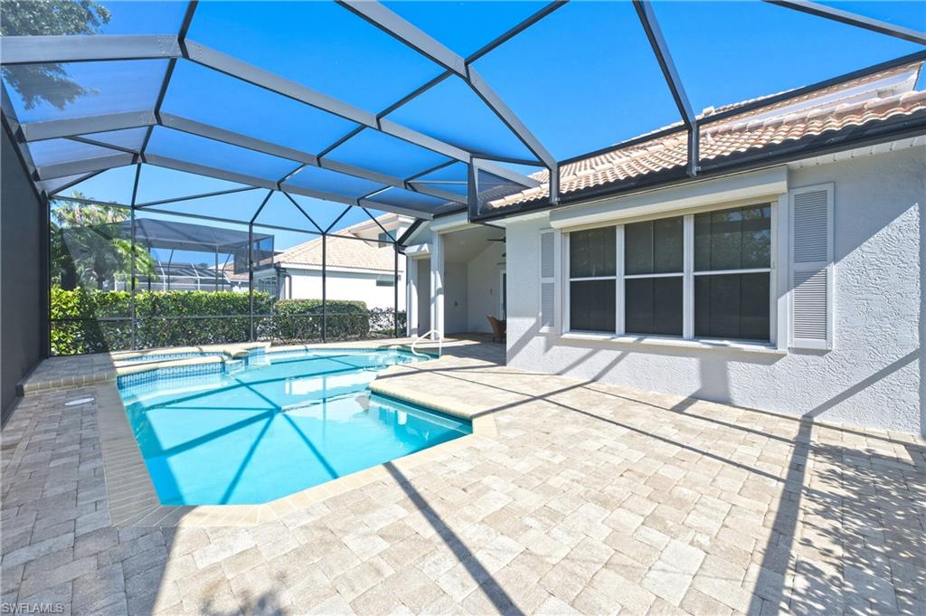 1960 Timarron Way Naples, FL 34109 - Photo 34 of 45 Screened-in pool area featuring a rectangular swimming pool with an integrated spa, paver decking, and a stucco exterior with decorative shutters