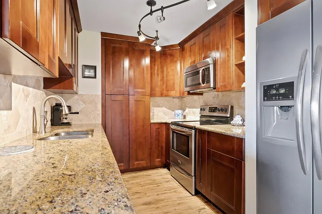 a kitchen with stainless steel appliances granite countertop a refrigerator a stove and a sink with wooden floor