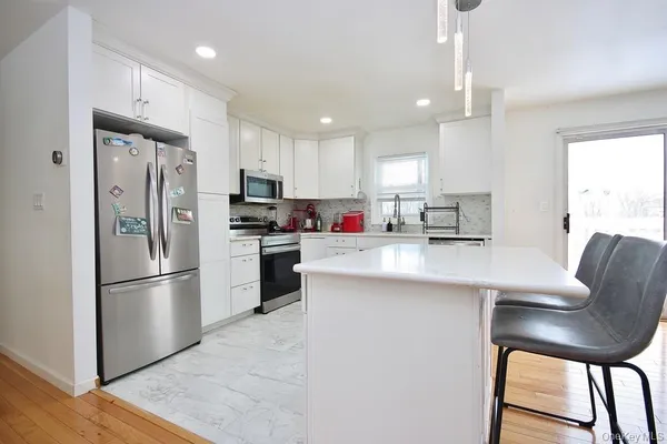 a kitchen with stainless steel appliances granite countertop a refrigerator a stove a sink a dining table and chairs with wooden floor