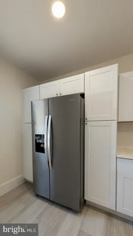 a view of a refrigerator in kitchen and an empty room with wooden floor